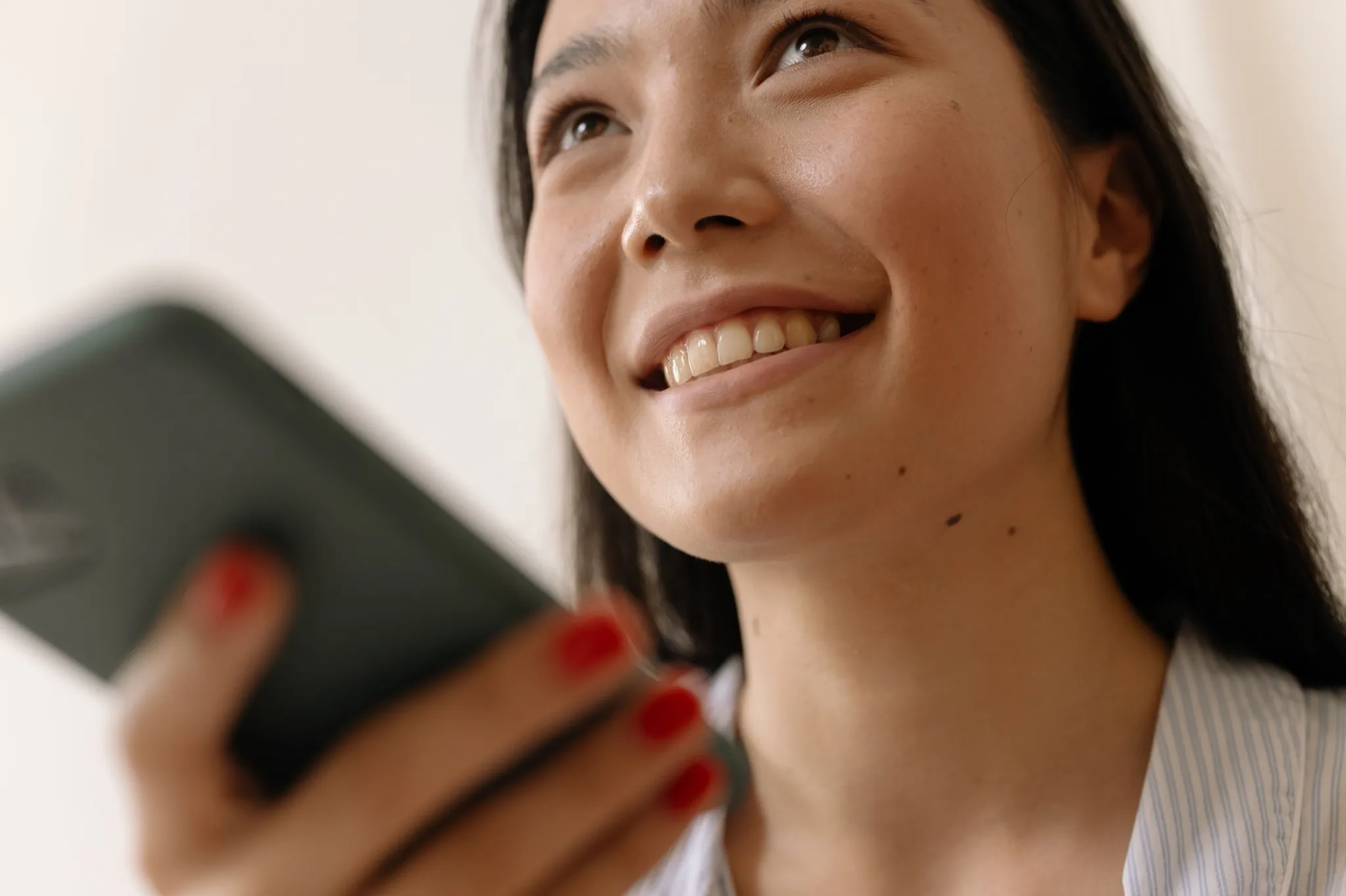 A young woman smiling while looking at her phone, reflecting a moment of connection and wellbeing.